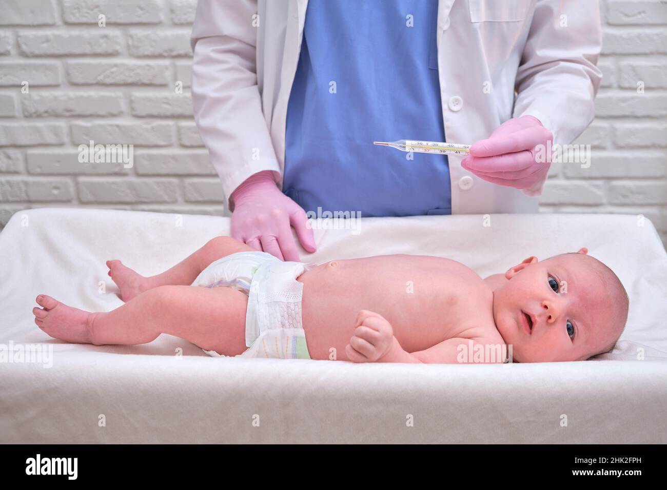 Doctor checks the temperature of the newborn baby with a thermometer. A nurse in uniform measures the child fever with a thermometer Stock Photo