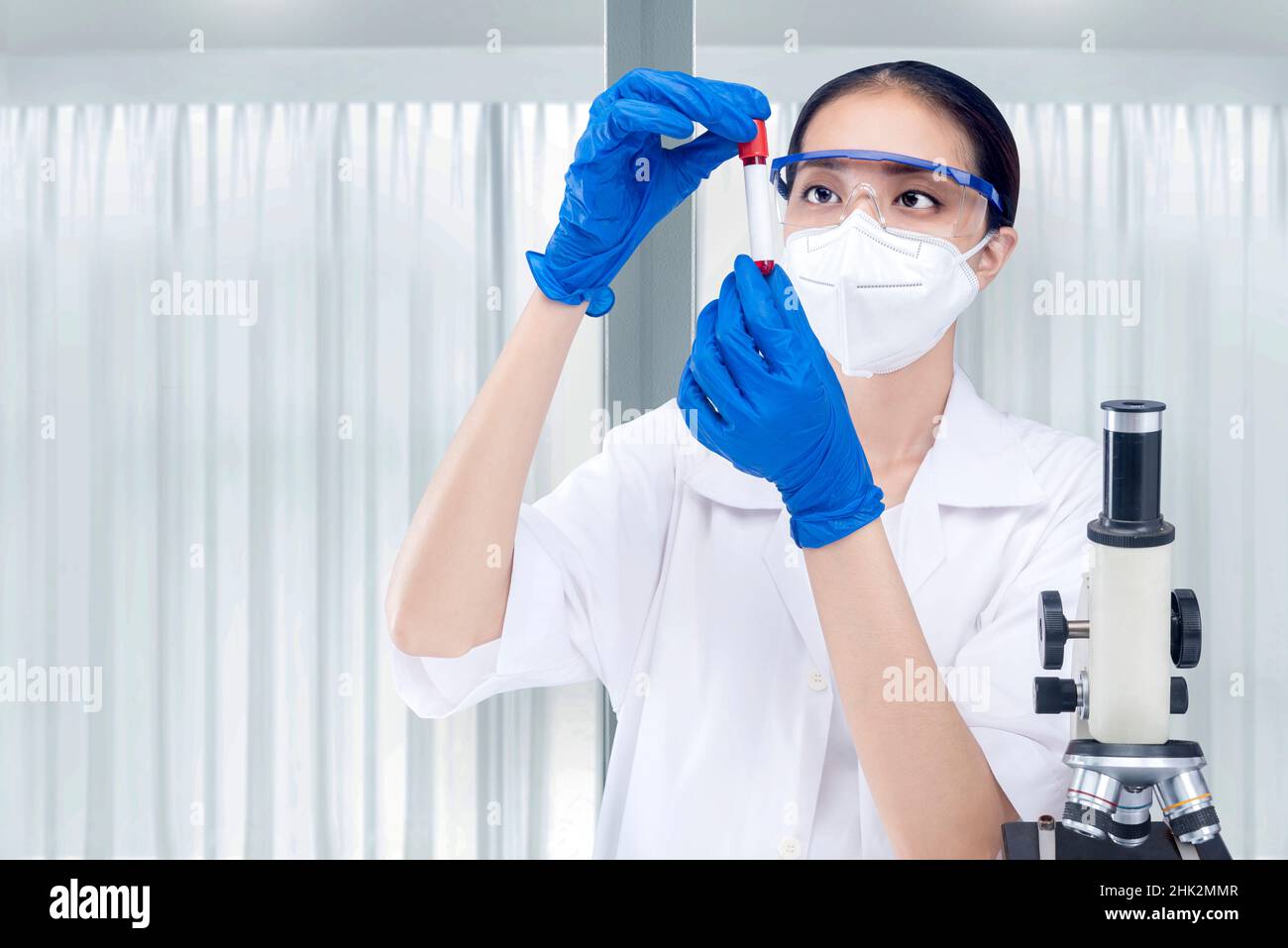 Asian researcher woman with face mask and glasses holding medical tube on the lab Stock Photo