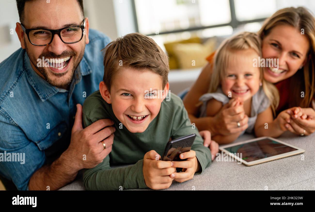Happy young family having fun time at home. Parents with children using digital device. Stock Photo