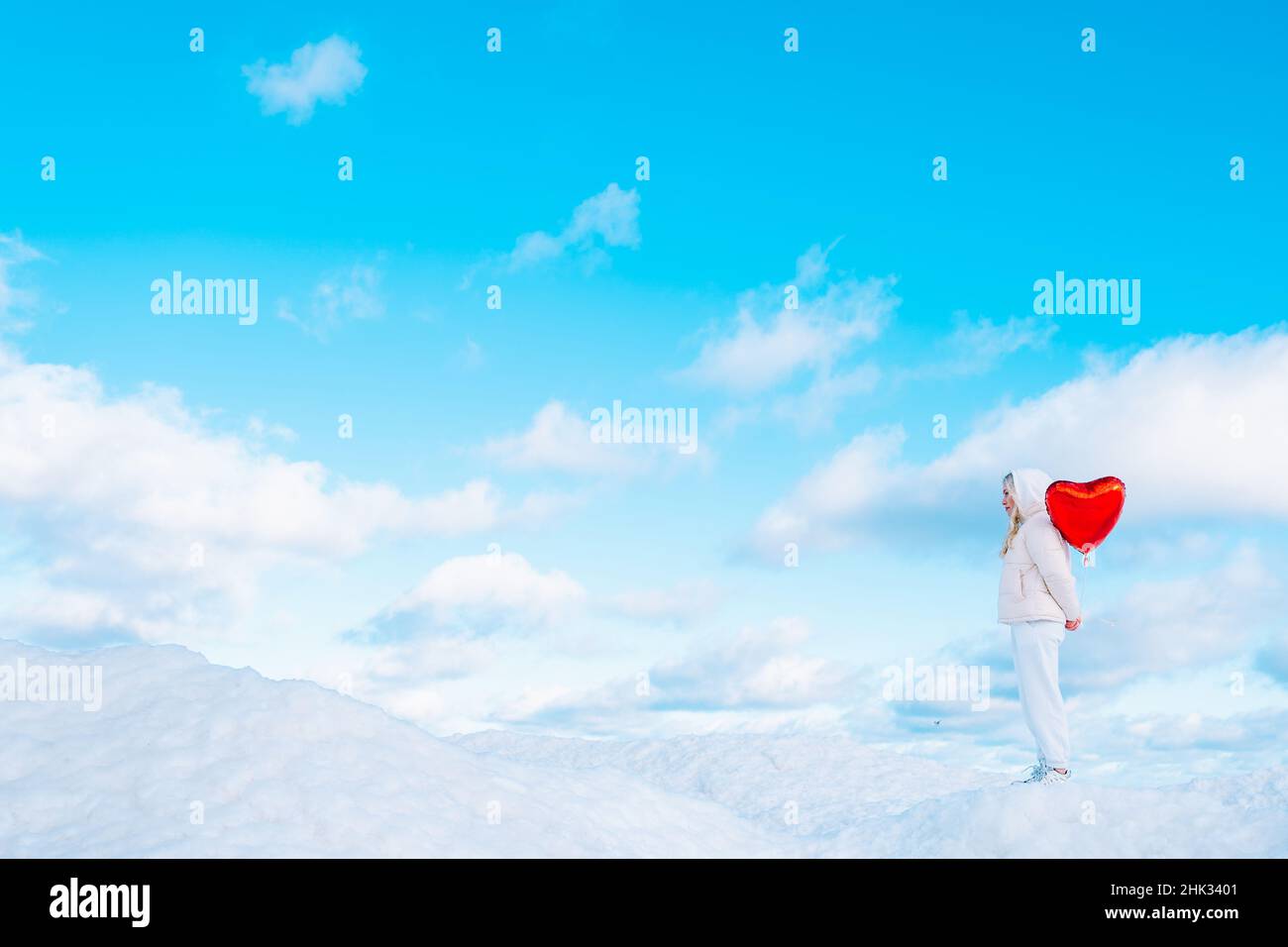 Woman with red heart-shaped balloon standing alone on snow covered hill Stock Photo