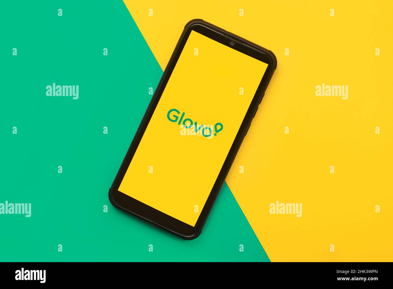Glovo application icon on black screen of smartphone over yellow and green background. Food delivery app Stock Photo