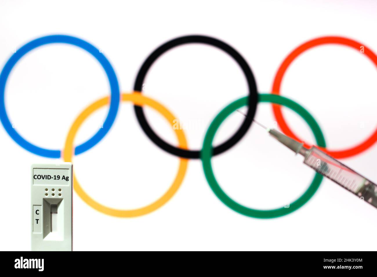 In this photo illustration a covid-19 antigene rapid test and a medical syringe seen in front of the olympic games logo. Stock Photo