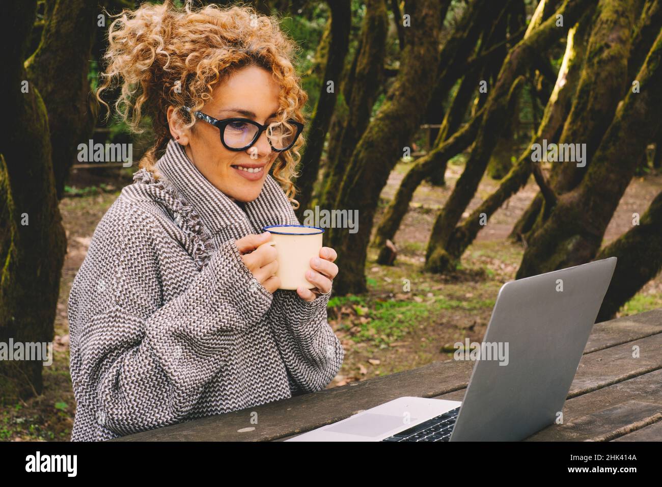 Attractive adult woman use laptop computer outdoor sitting in the trees ...
