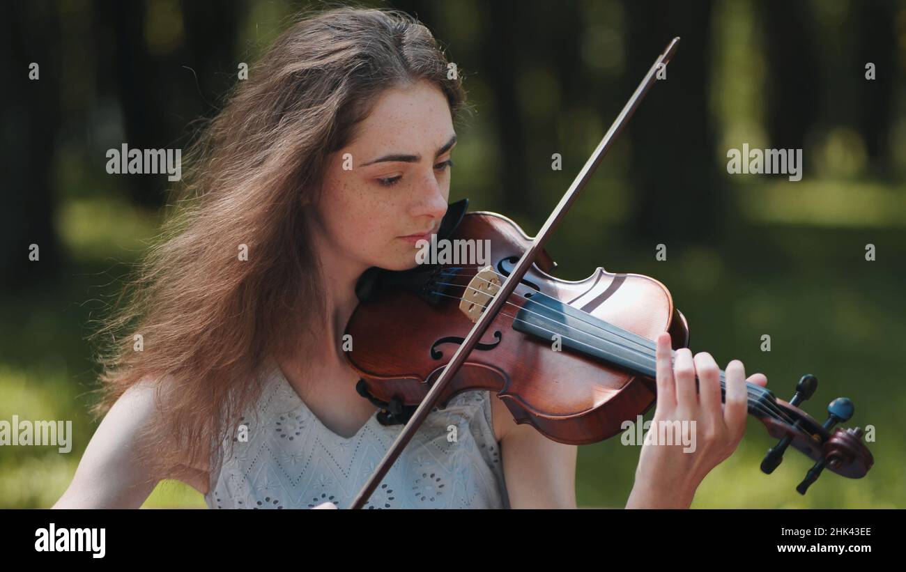 A young girl plays the violin in the city park. Stock Photo