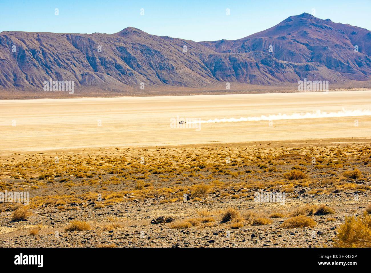 USA, Nevada, Vehicle Leaving Dusty Wake on Dusty Black Rock Desert Playa framed by Burnt Rock Peak Stock Photo