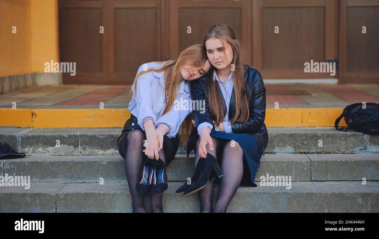 Tired schoolgirls sit barefoot on the steps of the school. Stock Photo