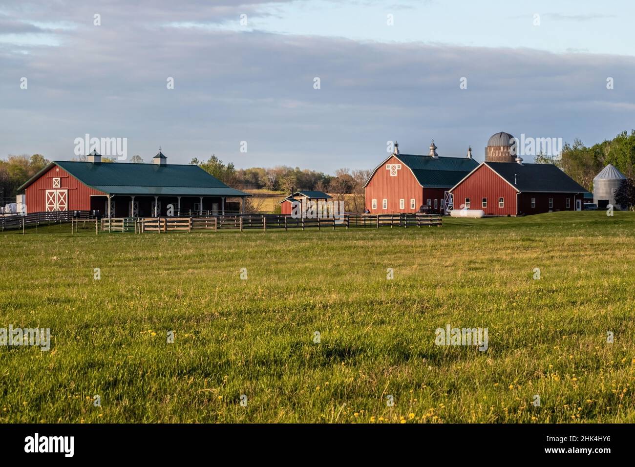 Red barns and silos with fencing taken across a grassy meadow as the sun was getting low in the sky. Stock Photo