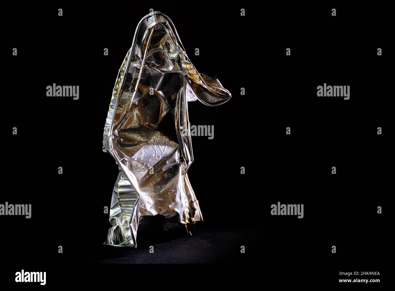 Aluminum foil tray of convenience food shown like a human art sculpture against a black background, avoidable waste from disposable packaging use reso Stock Photo