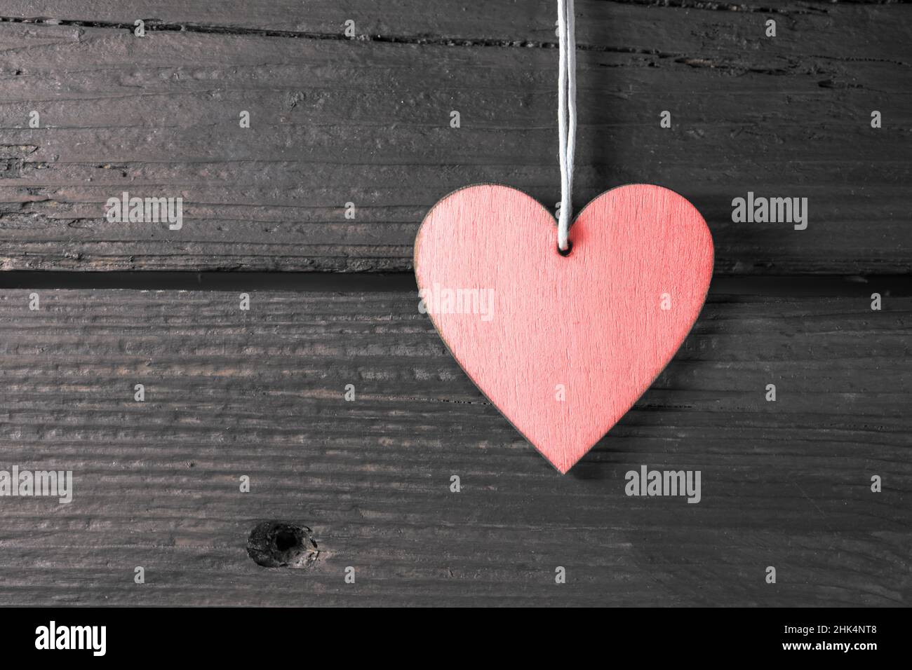 Pink heart shape hanger on a dark rustic wood wall, symbol of love in everyday life and holidays like valentines, mother's day, father's day and birth Stock Photo