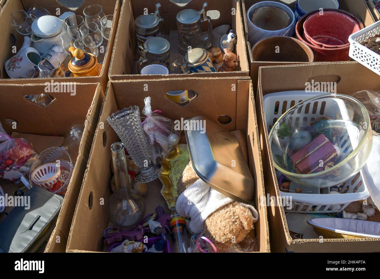 Cardboard boxes with old used household items and tableware on a garage sale or flea market at a 
