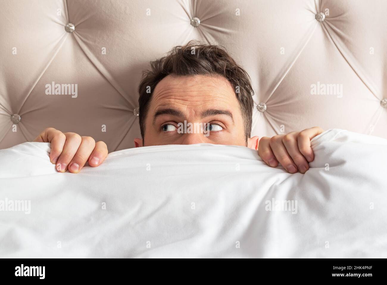 Caucasian young man hiding in bed under the blanket at home. He is stressed and tries run away from problems. Stock Photo