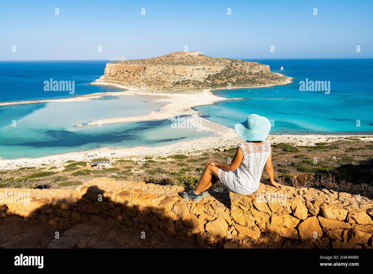 Charming woman with sundress and hat contemplating the crystal turquoise sea and lagoon, Balos, Crete, Greek Islands, Greece, Europe Stock Photo