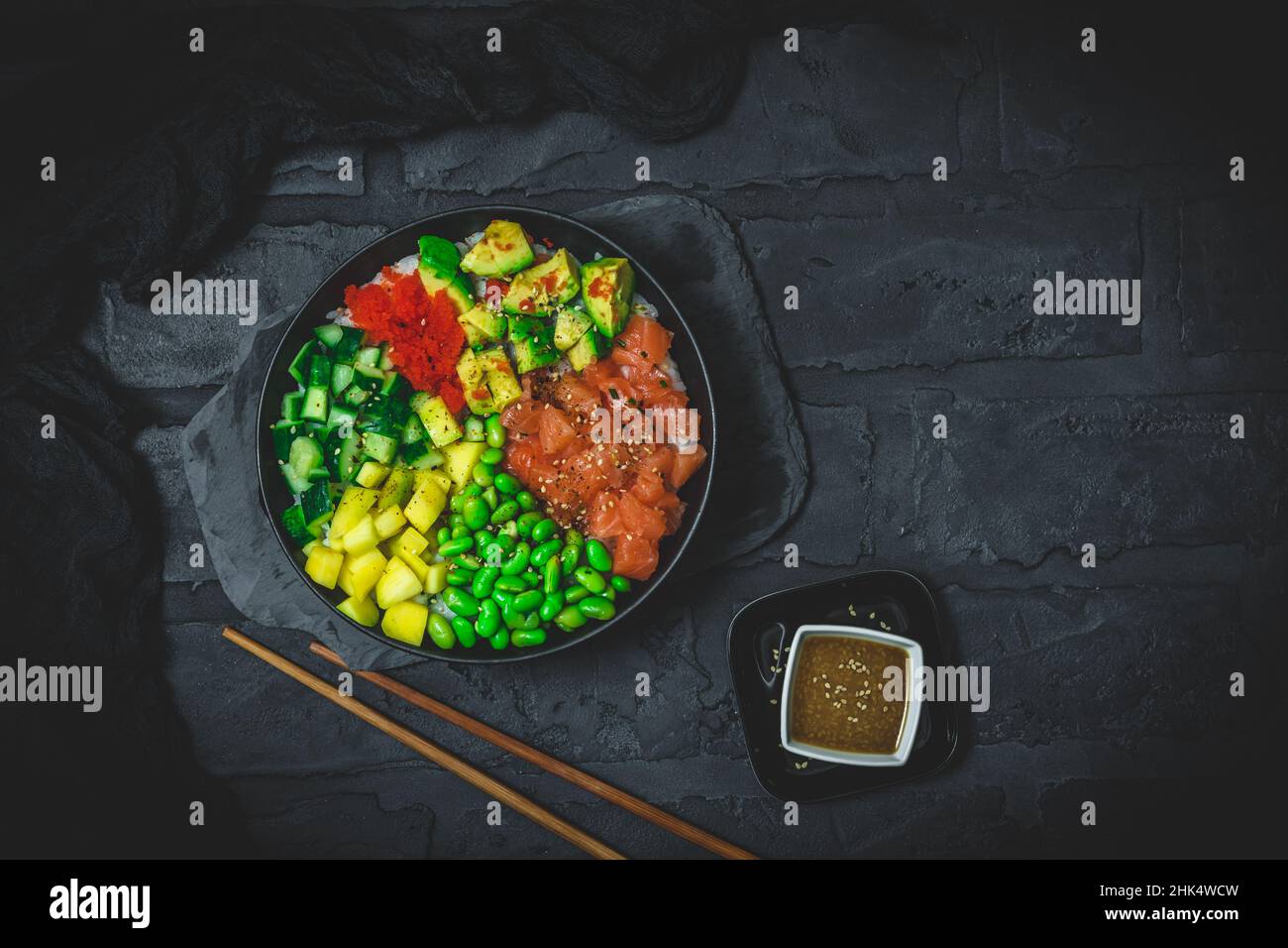 Japanese poke or buddha bowl with salmon, avocado, roe, mango, pies and cucumber in a black bowl on black background, top view with copy space Stock Photo