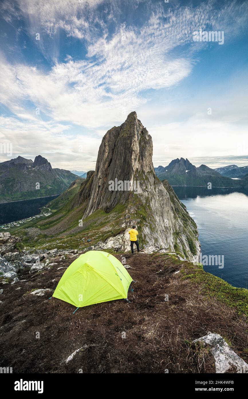 Hiker man with camping tent admiring Mount Segla and fjord from Hesten peak at sunset, Senja, Troms county, Norway, Scandinavia, Europe Stock Photo