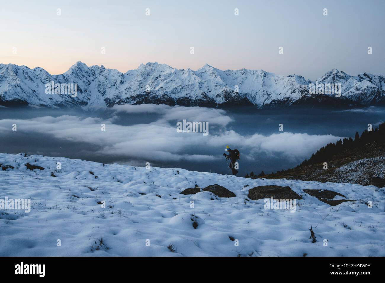 Man with hiking poles walking in the snow with majestic Orobie Alps in the background, Alpe Rogneda, Rhaetian Alps, Lombardy, Italy, Europe Stock Photo