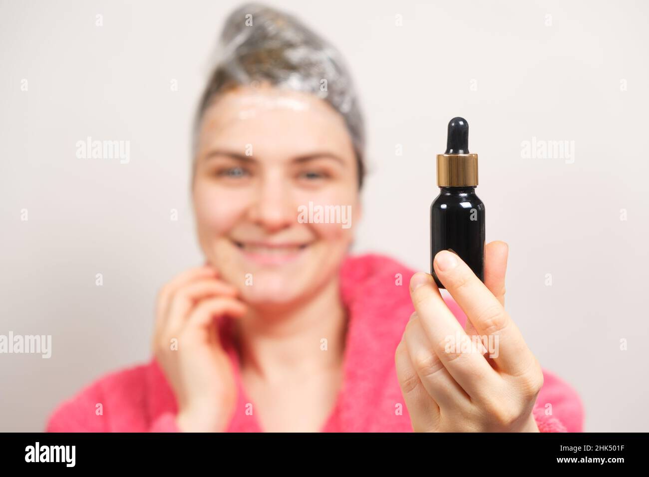 A woman with a film on her head holds a bottle of natural hair oil. Hair care at home, preparations for hair growth Stock Photo