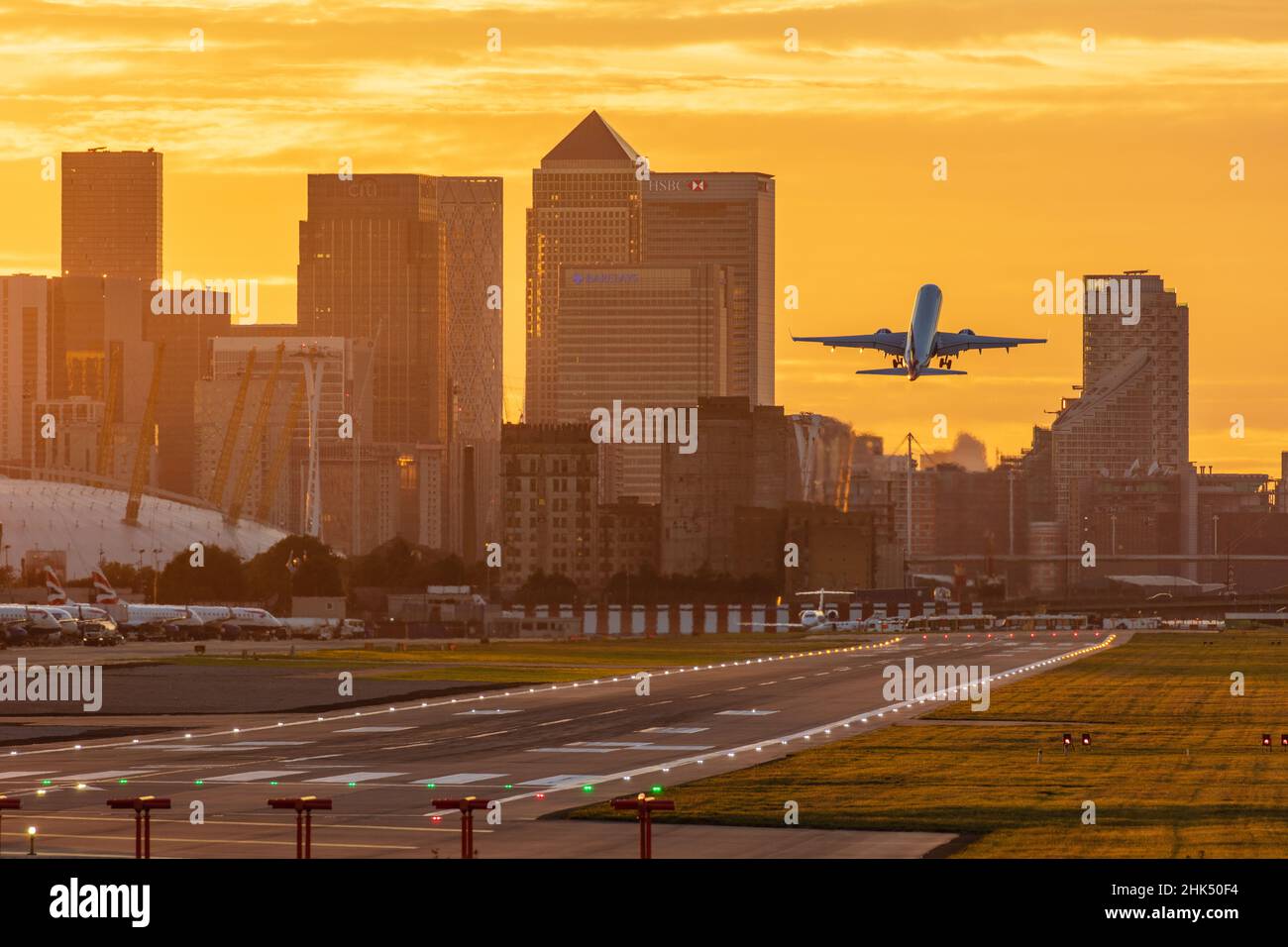 Aircraft taking off from London City Airport at sunset, with Canary Wharf and O2 Arena in background, London, England, United Kingdom, Europe Stock Photo