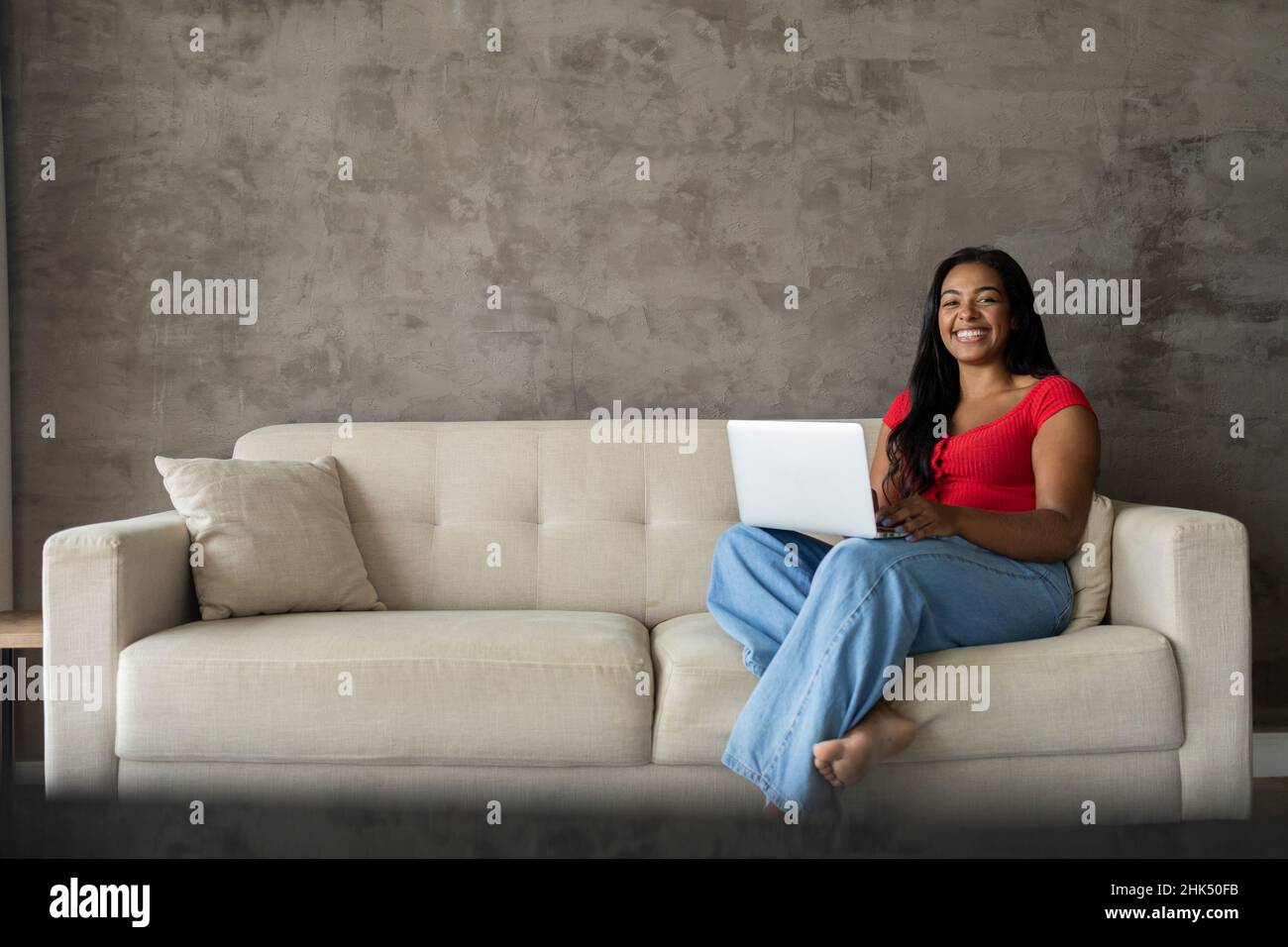Young black woman working at home with laptop on her lap sitting on her ...