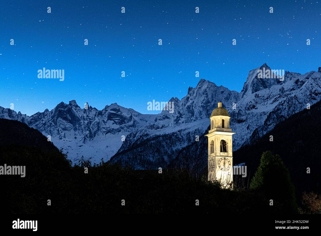 Illuminated bell tower and Sciore mountain range covered with snow under the starry sky, Soglio, Graubunden, Switzerland, Europe Stock Photo