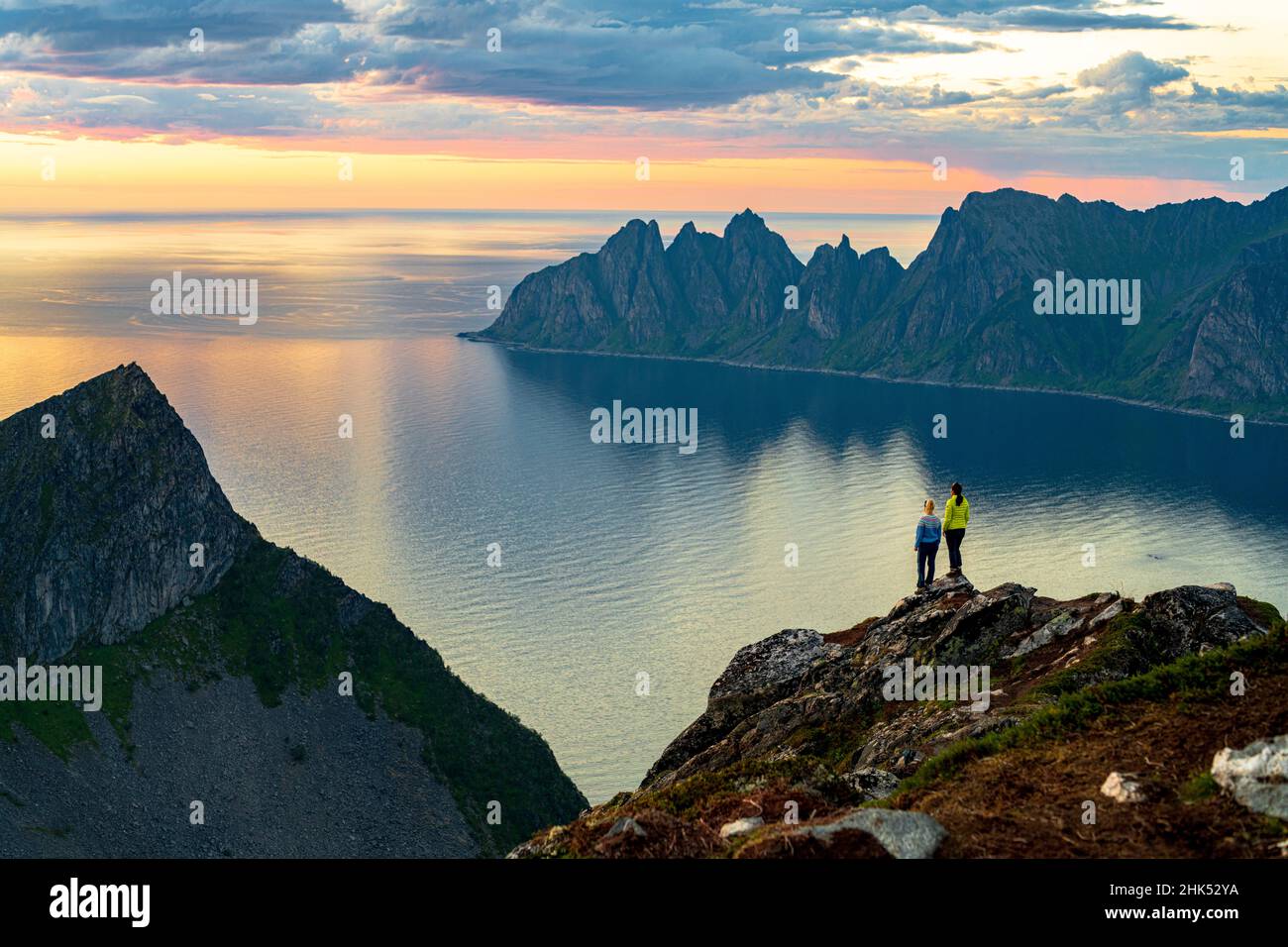 Two young women watching sunset standing on mountain top, Senja island, Troms county, Norway, Scandinavia, Europe Stock Photo