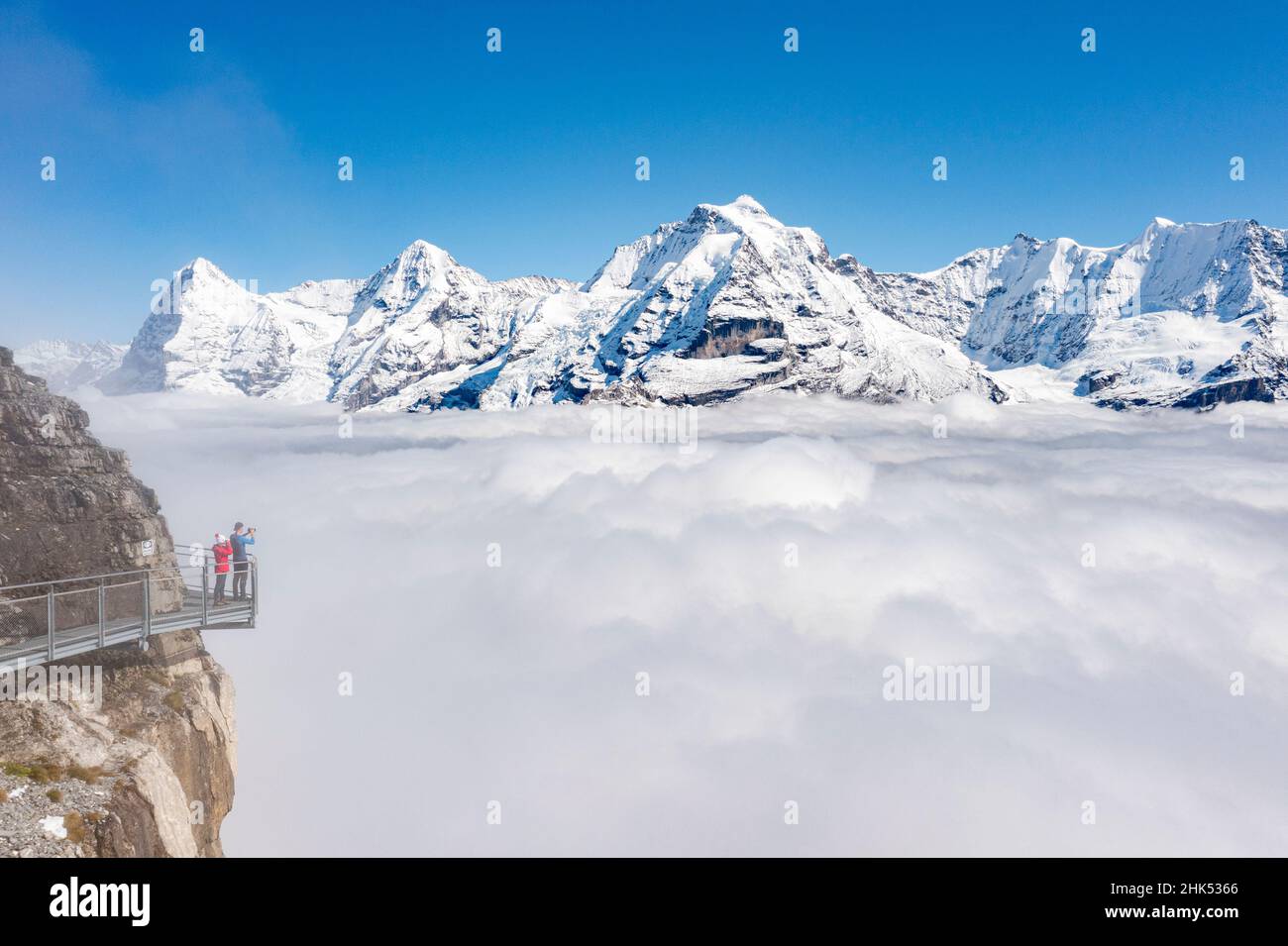 Two people photographing snowcapped Eiger and Monch peaks in fog from elevated walkway, Murren Birg, Bern canton, Swiss Alps, Switzerland, Europe Stock Photo