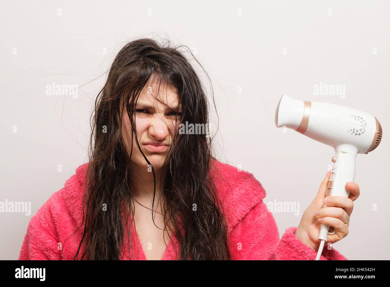 A brunette woman with matted hair dries it with a hair dryer. Hair care, overdried hair Stock Photo
