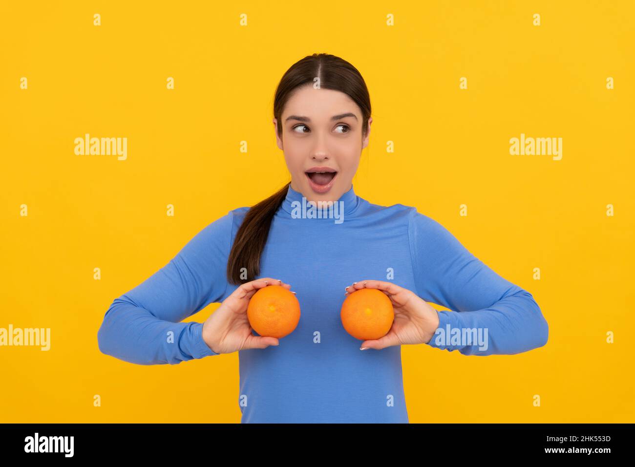 surprised young woman holding orange citrus fruit on yellow background, natural food Stock Photo