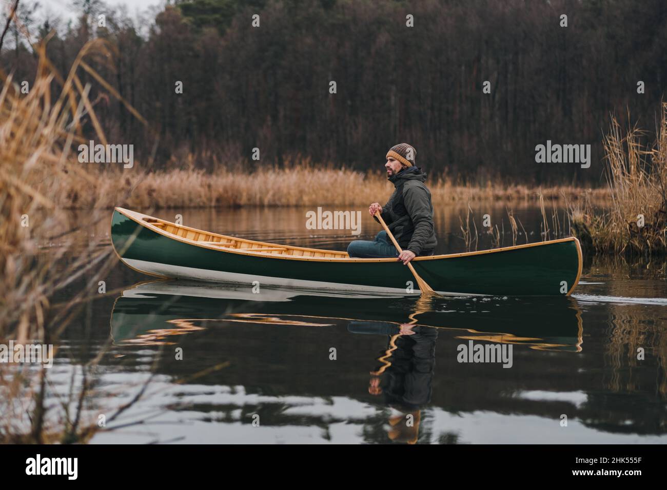 Man paddling a beautiful green canoe on the pond, calm late autumn nature. Active lifestyle, a person enjoying tranquil early spring scenery on the wa Stock Photo