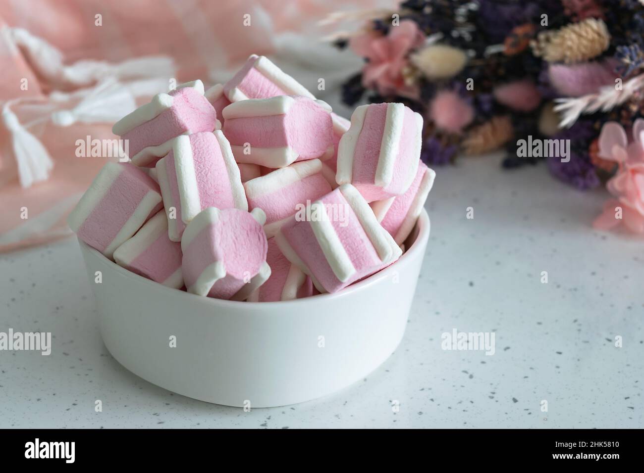 Marshmallow on a light table next to a bouquet of wild field dried flowers. Sweets for tea and coffee on a porcelain plate. Horizontal photo. Stock Photo