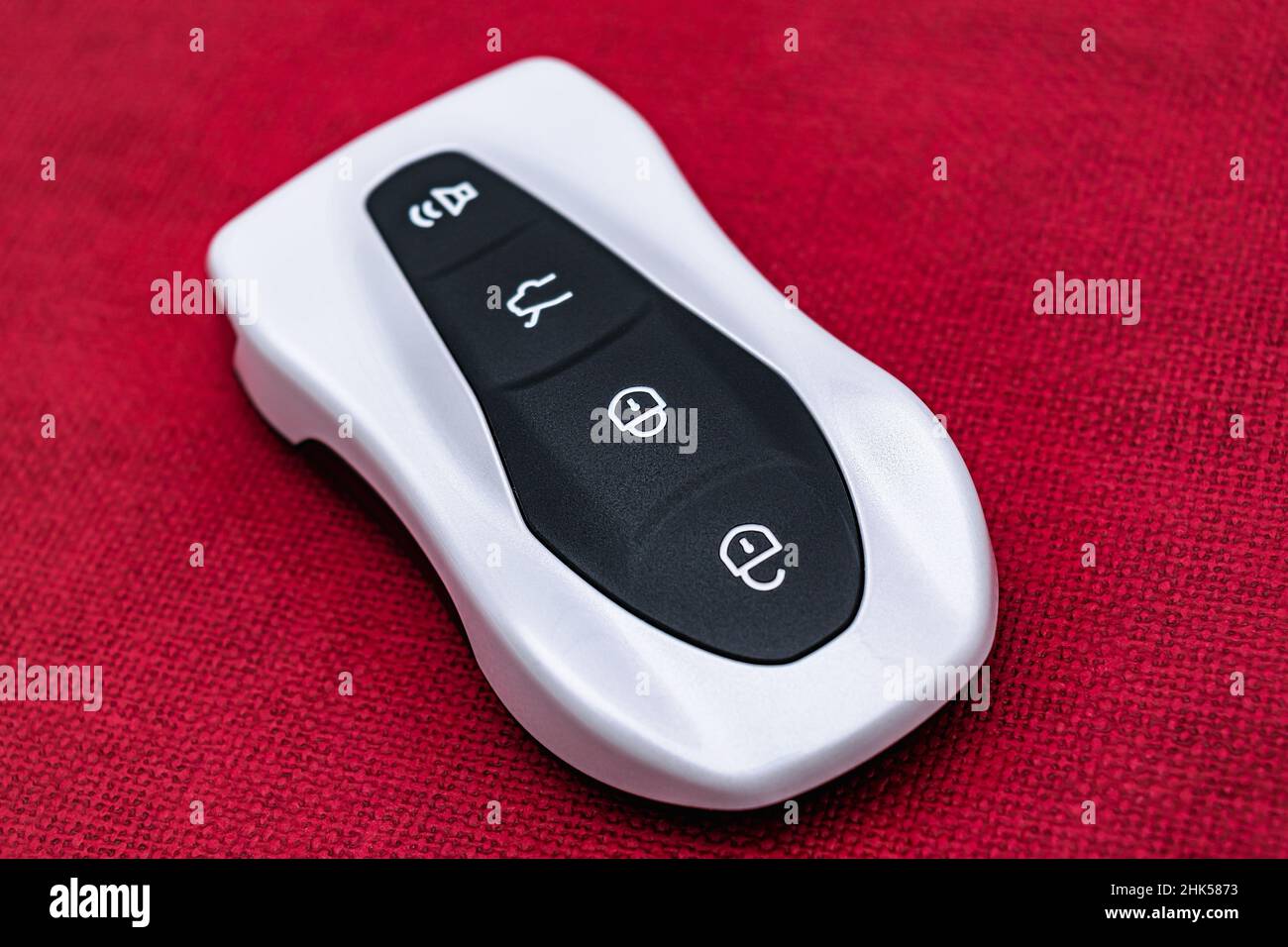 Close-up of a white-black smart car key on a red embossed background. Electronics, spare parts and car accessories. Horizontal photo. Stock Photo