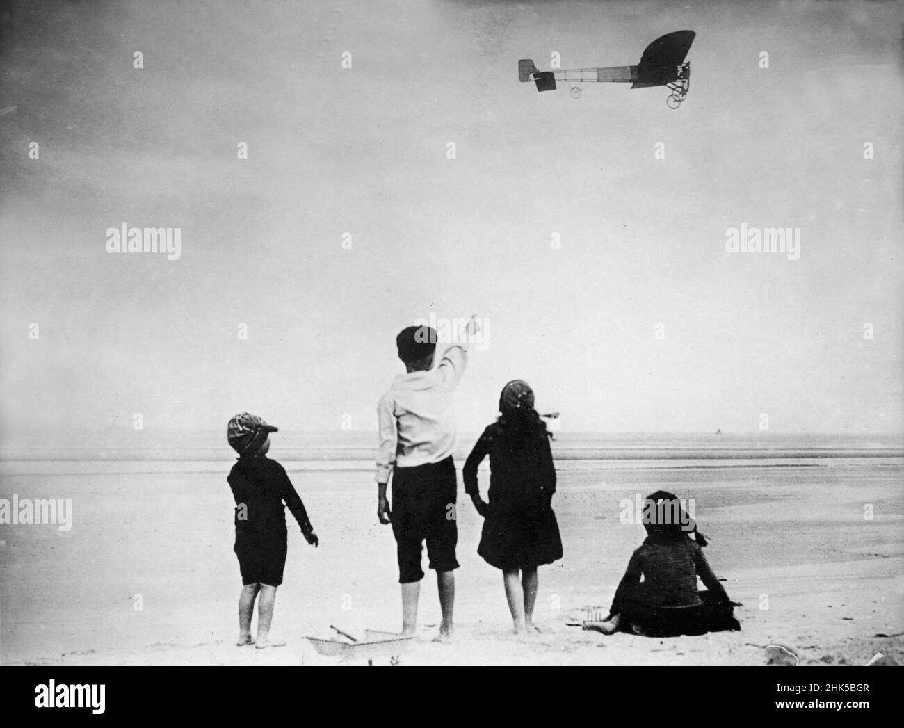 Vintage photo dated July 25th 1909 of the French aviation pioneer Louis Bleriot flying his Bleriot Type XI monoplane on the first crossing of the English Channel passing over the beach at Calais being watched by children Stock Photo