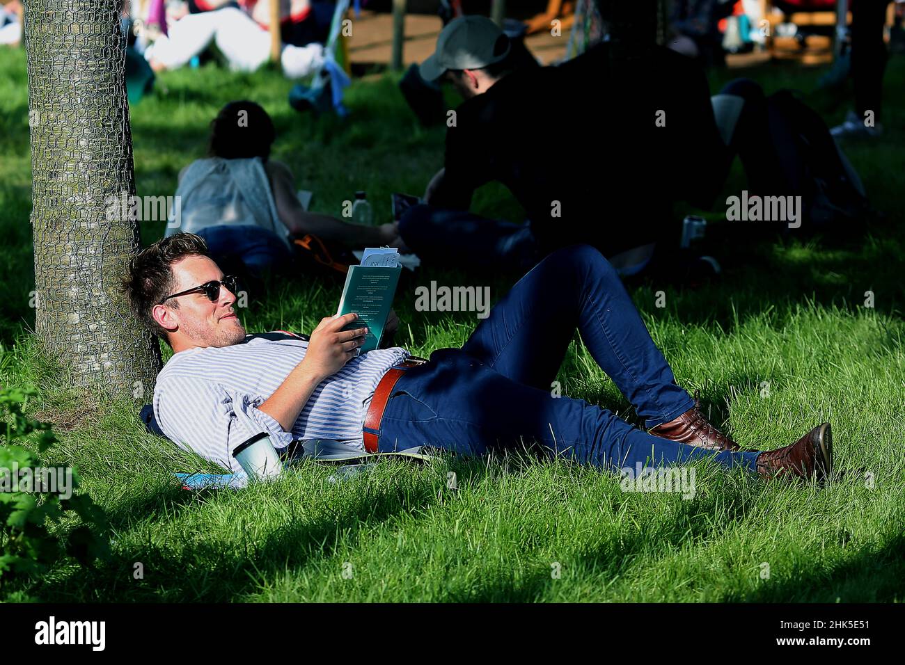 Hay Festival, a man reads a book in the sun under a tree on the green on the 27th of May 2018. Stock Photo