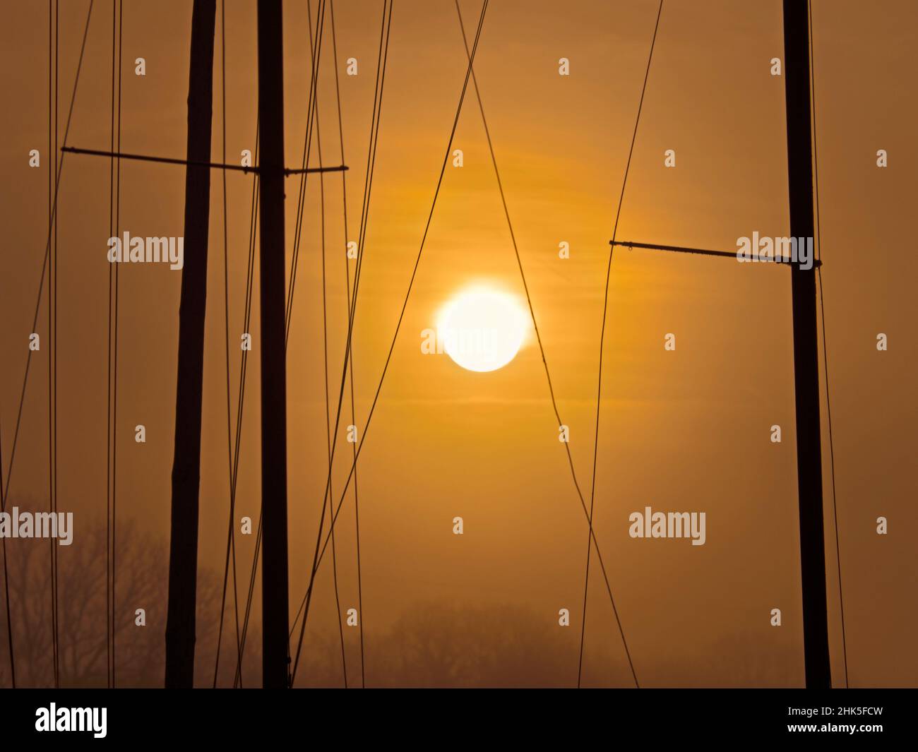 Big, orange sun; an abstract array of yacht masts at sunrise in Abingdon Marina by the Thames. Stock Photo
