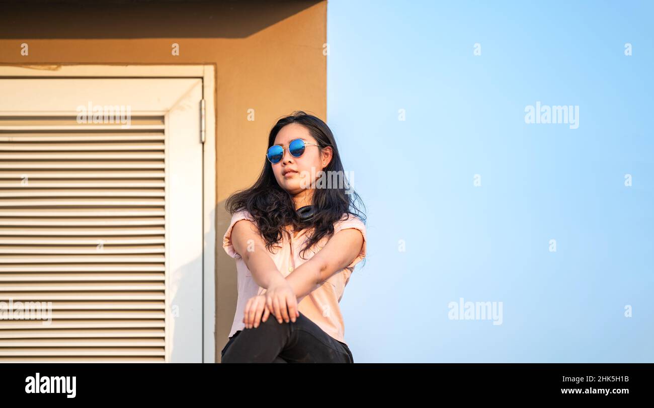 Sun Glasses Asian woman is sitting on the rooftop barricade cement (not dangerous because the opposite site is rooftop floor as well) in front of empt Stock Photo