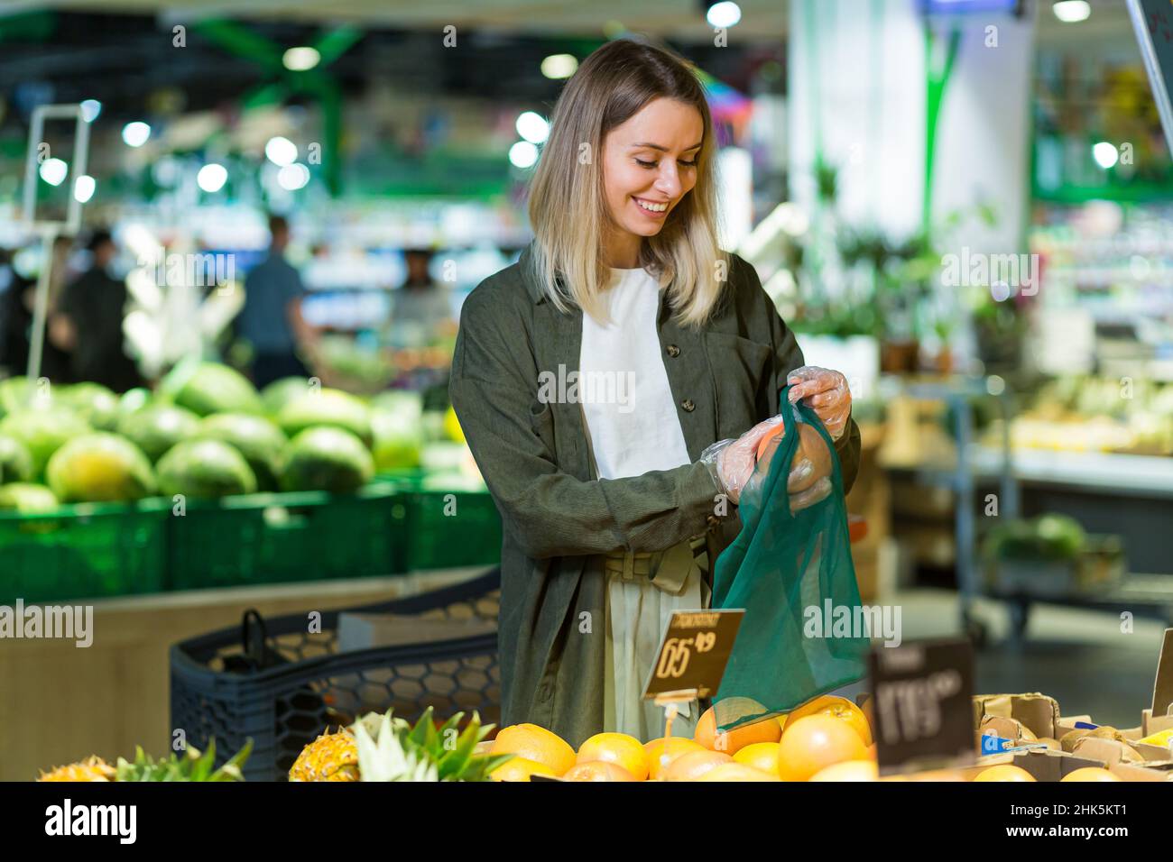 young woman chooses and picks in eco bag vegetables or fruits Oranges