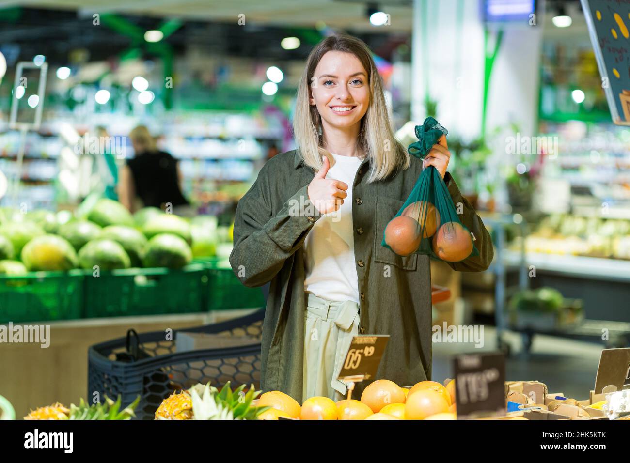 young woman chooses and picks in eco bag vegetables or fruits Oranges