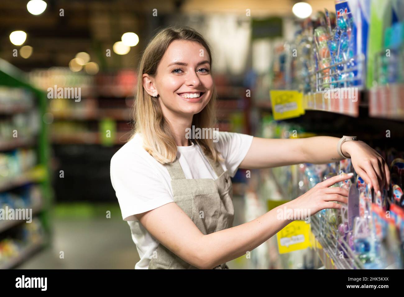 portrait of saleswoman, woman smiling and looking at camera in supermarket. Pleasant friendly female seller standing in the store between the rows . T Stock Photo