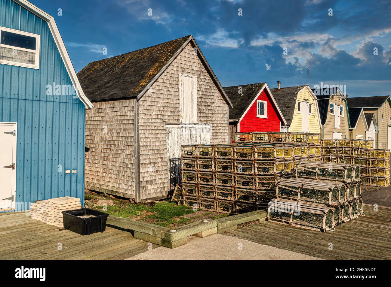 Lobster traps piled up on a wharf in front of colorful bait sheds. Stock Photo