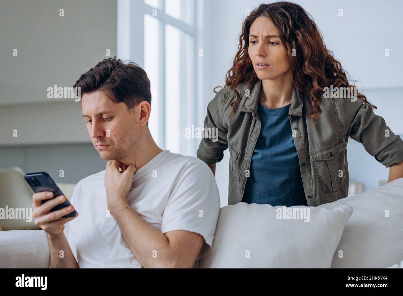 Young woman looks out over husband shoulder at phone screen and starts
