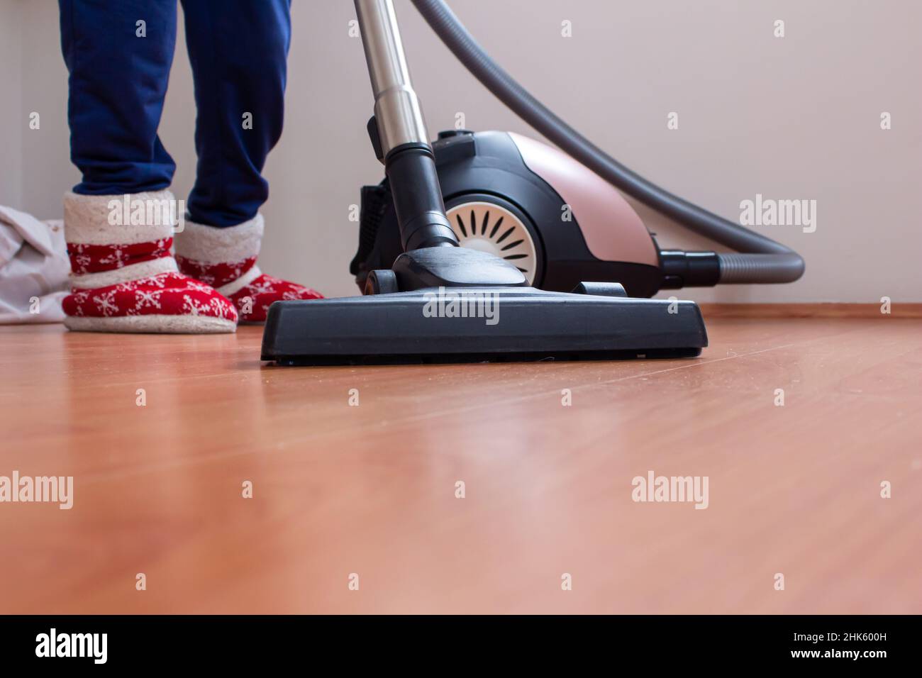 Woman using a vacuum cleaner to clean the parquet floor. She is cleaning the house where there is excess dust. Stock Photo