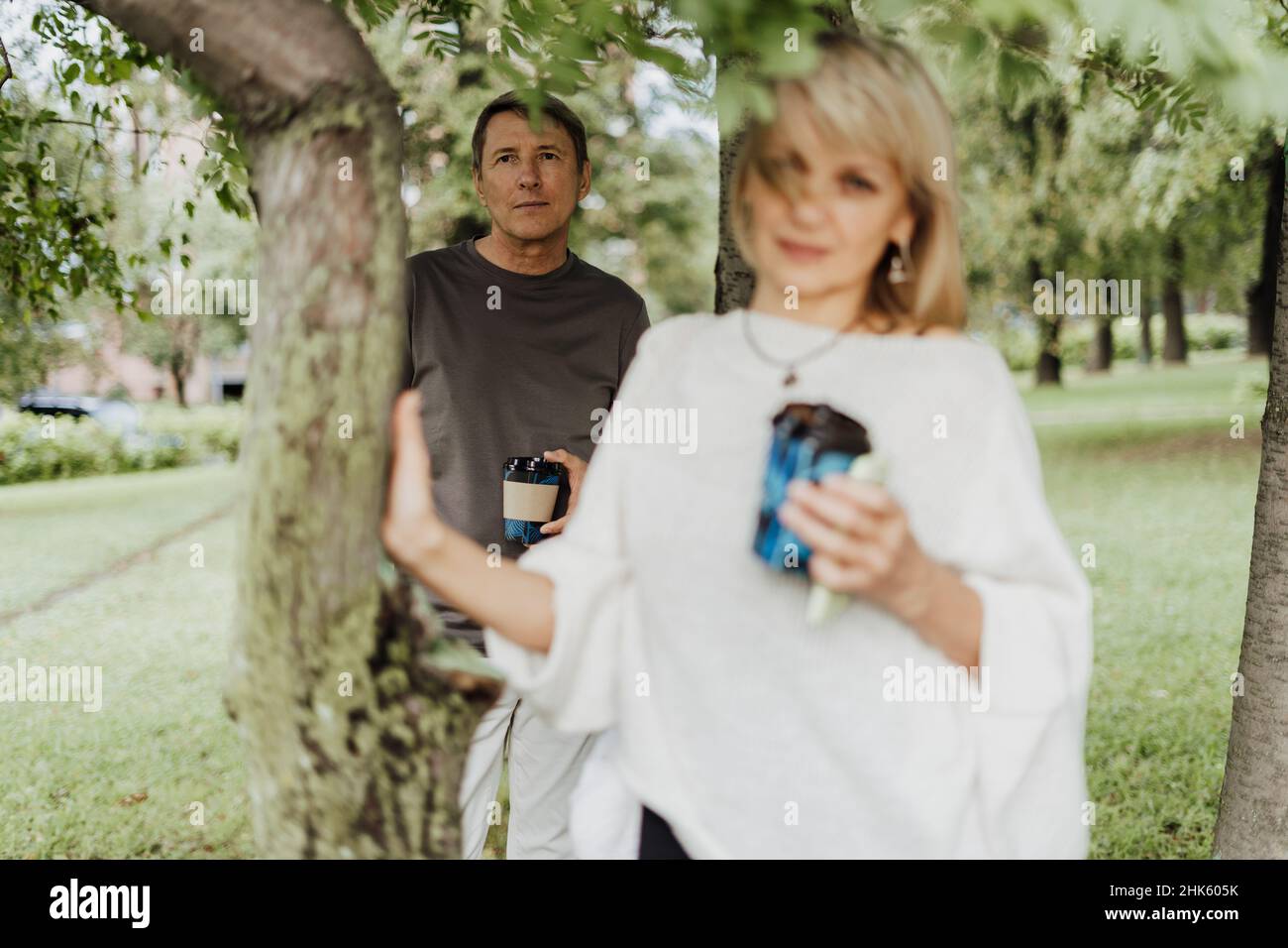 An adult mature happy couple in love hugging outdoors in city park. A blonde caucasian man and woman spend time together and drinking coffee. Senior Stock Photo