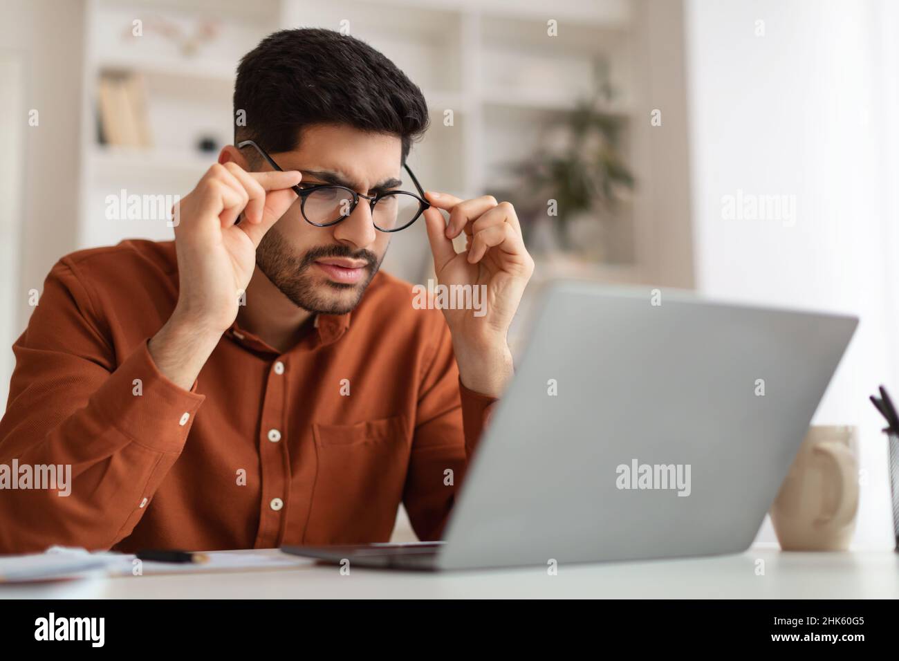 Confused Arab guy using laptop looking at screen Stock Photo