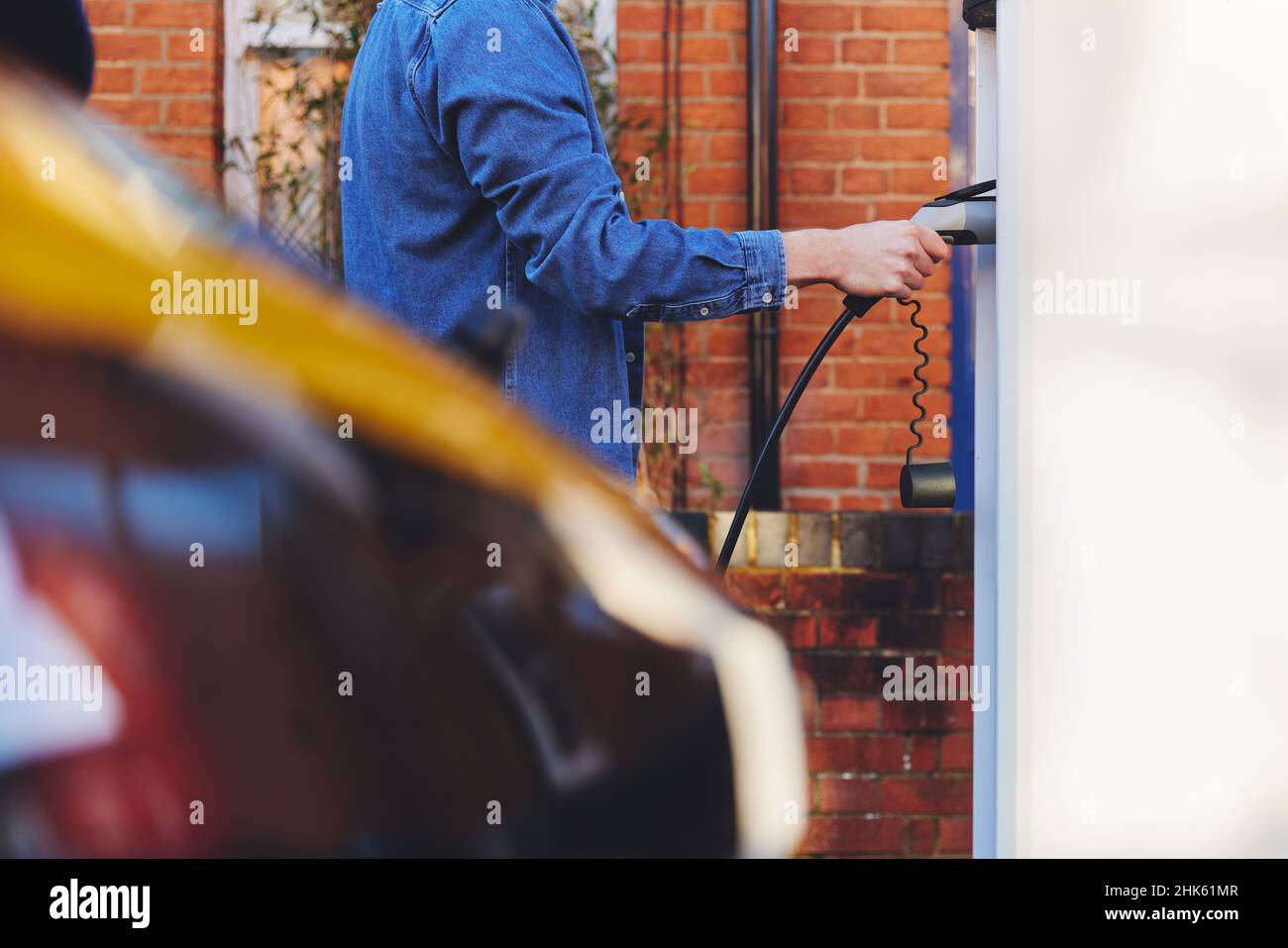 Man plugging in electric car to charging point outside home on street Stock Photo