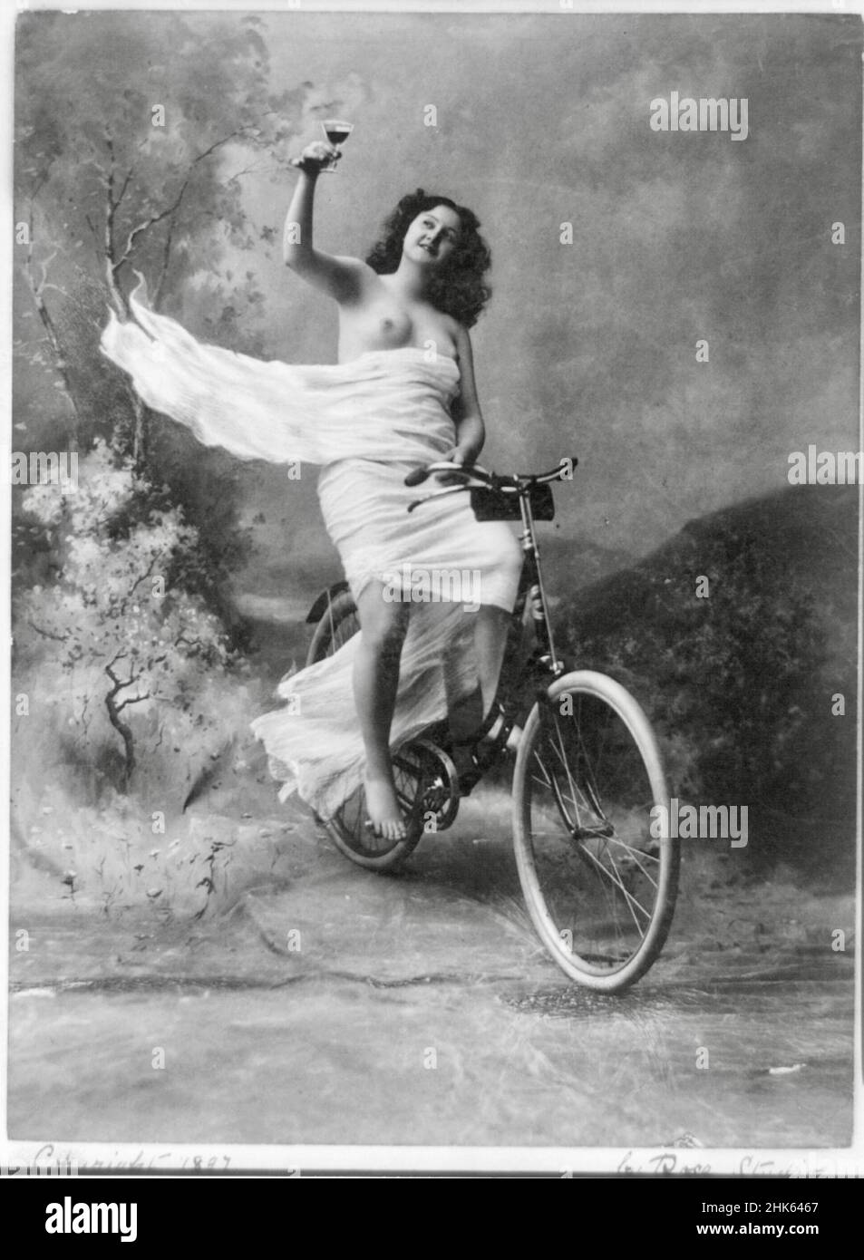 Queen of the Wheel - partially nude young woman, dressed in white flowing  material, sitting on a bicycle, holding a glass of wine - 1897 Stock Photo  - Alamy