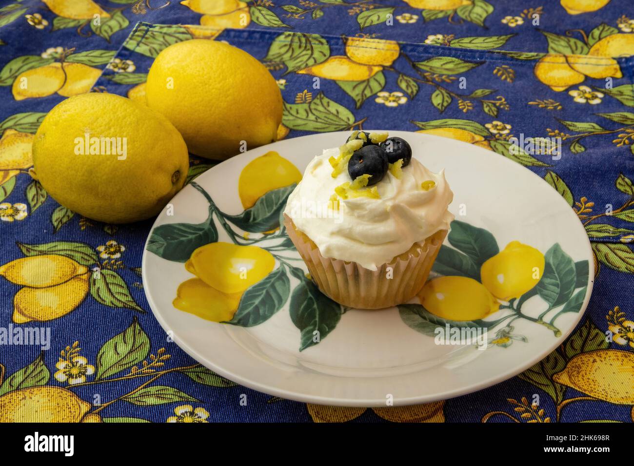 Lemon blueberry cupcake with blueberries and lemon zest with lemons and decorative lemon plate and tablecloth. Stock Photo