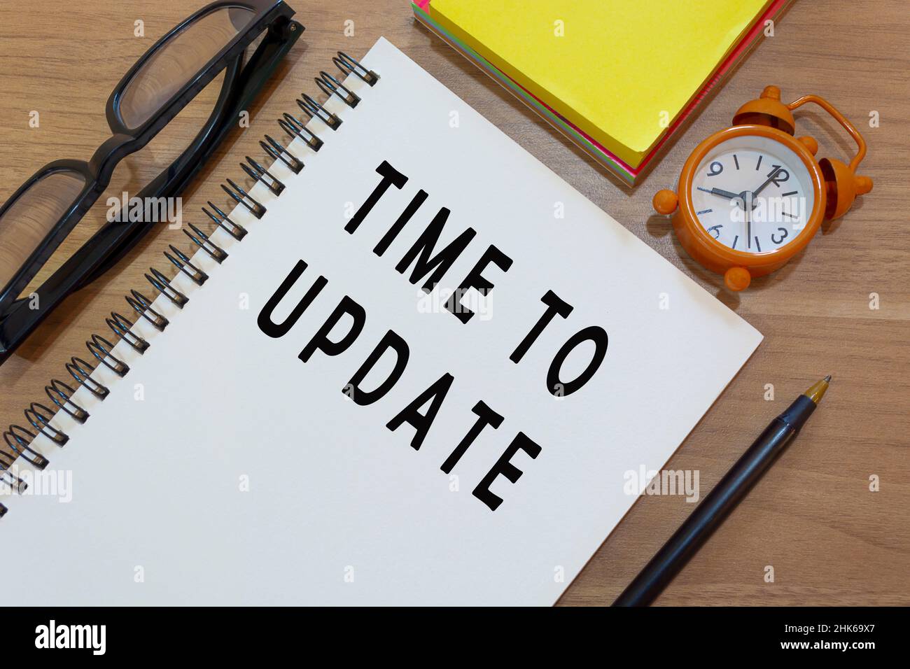 Time to update text on notepad with alarm clock on wooden desk. Time