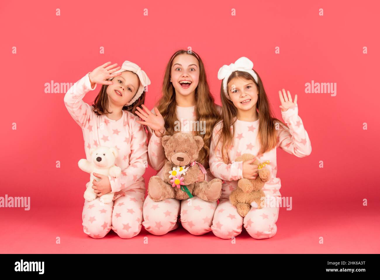 Hi there. Surprised children wave hands in pyjamas homewear. Girls sitting  together with teddy bears Stock Photo - Alamy