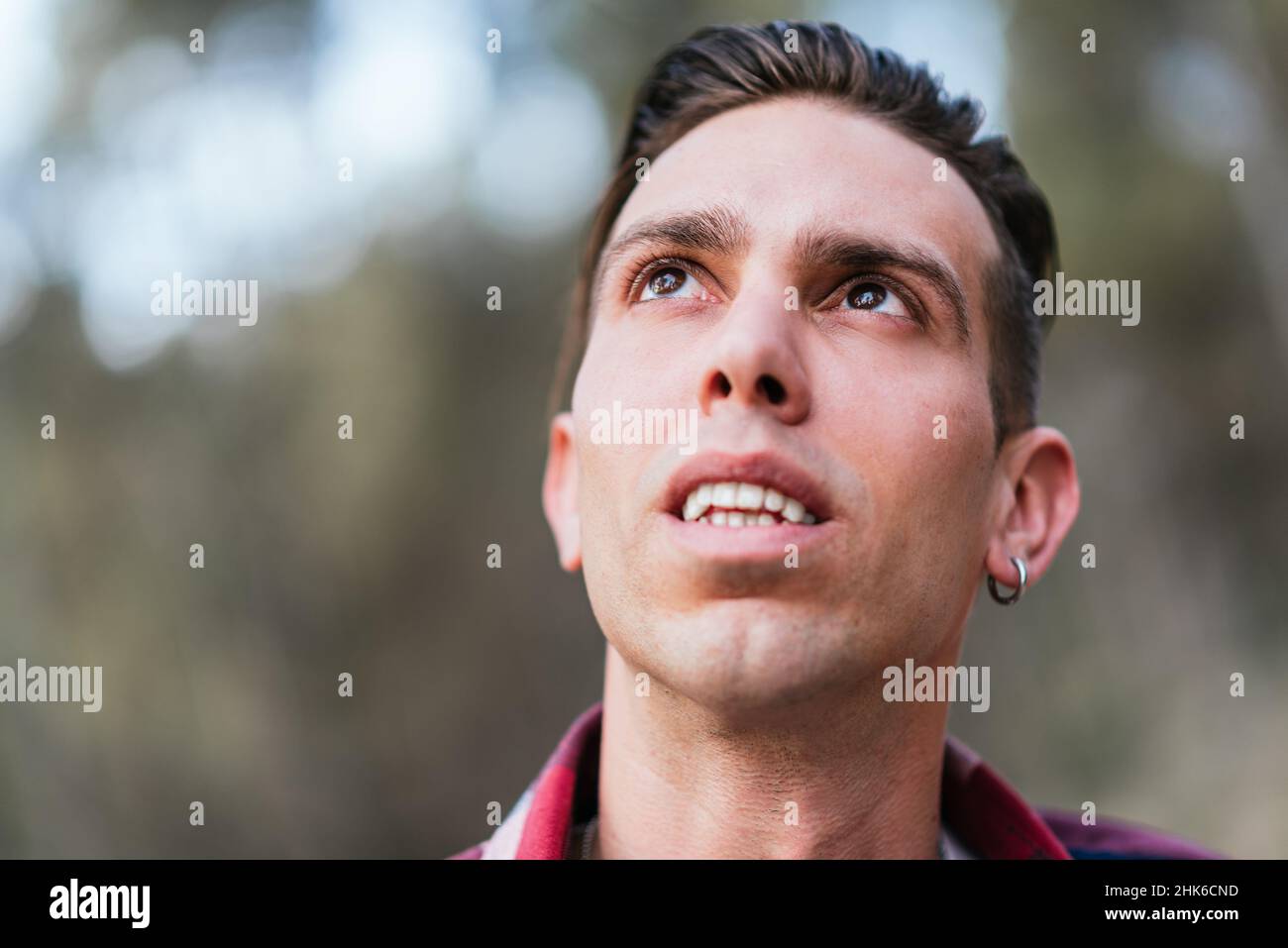 Serious male with ear piercing looking up with interest while spending day in nature Stock Photo