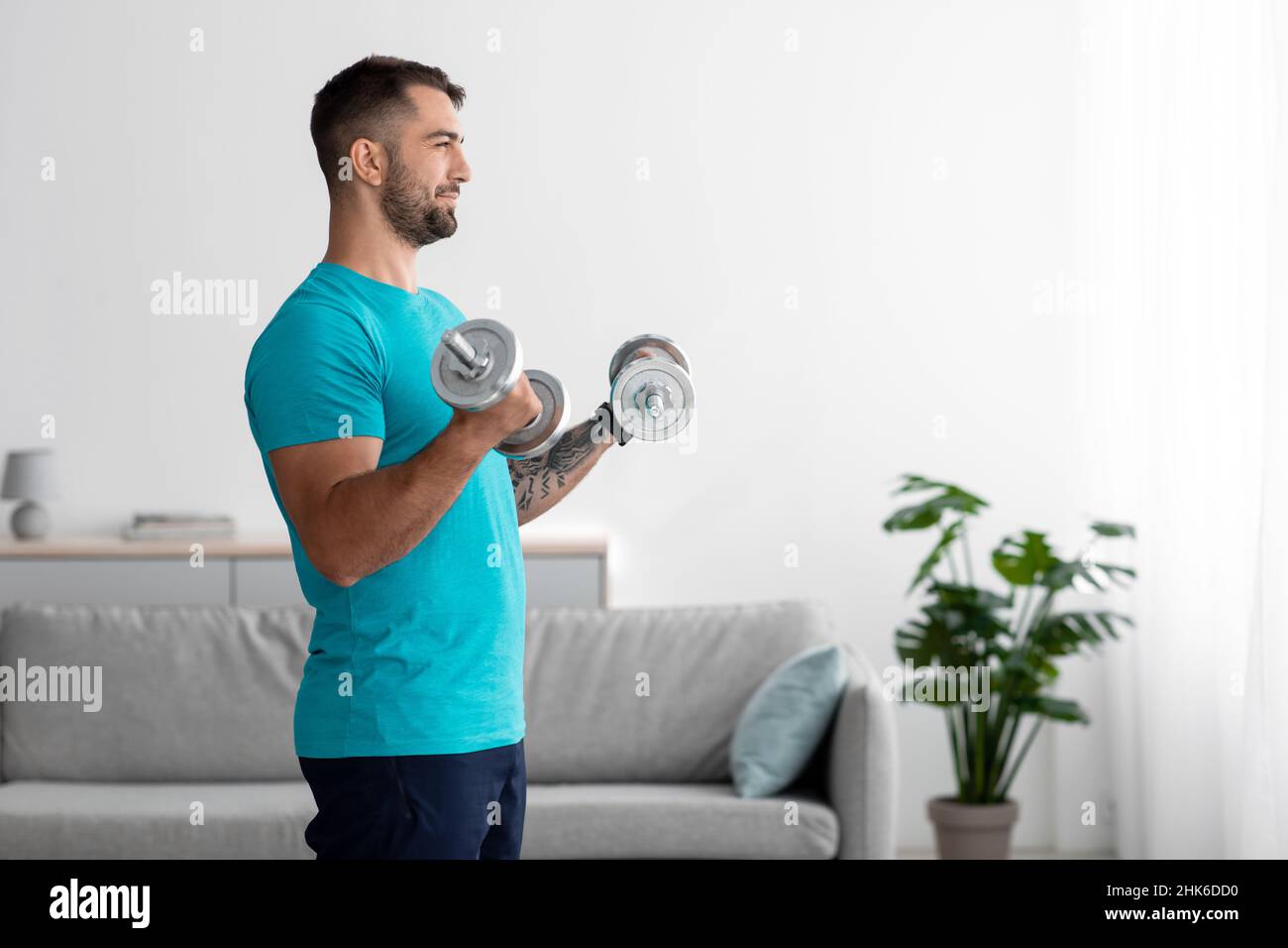 Cheerful handsome millennial muscular european man athlete doing arm exercises, lifts dumbbells