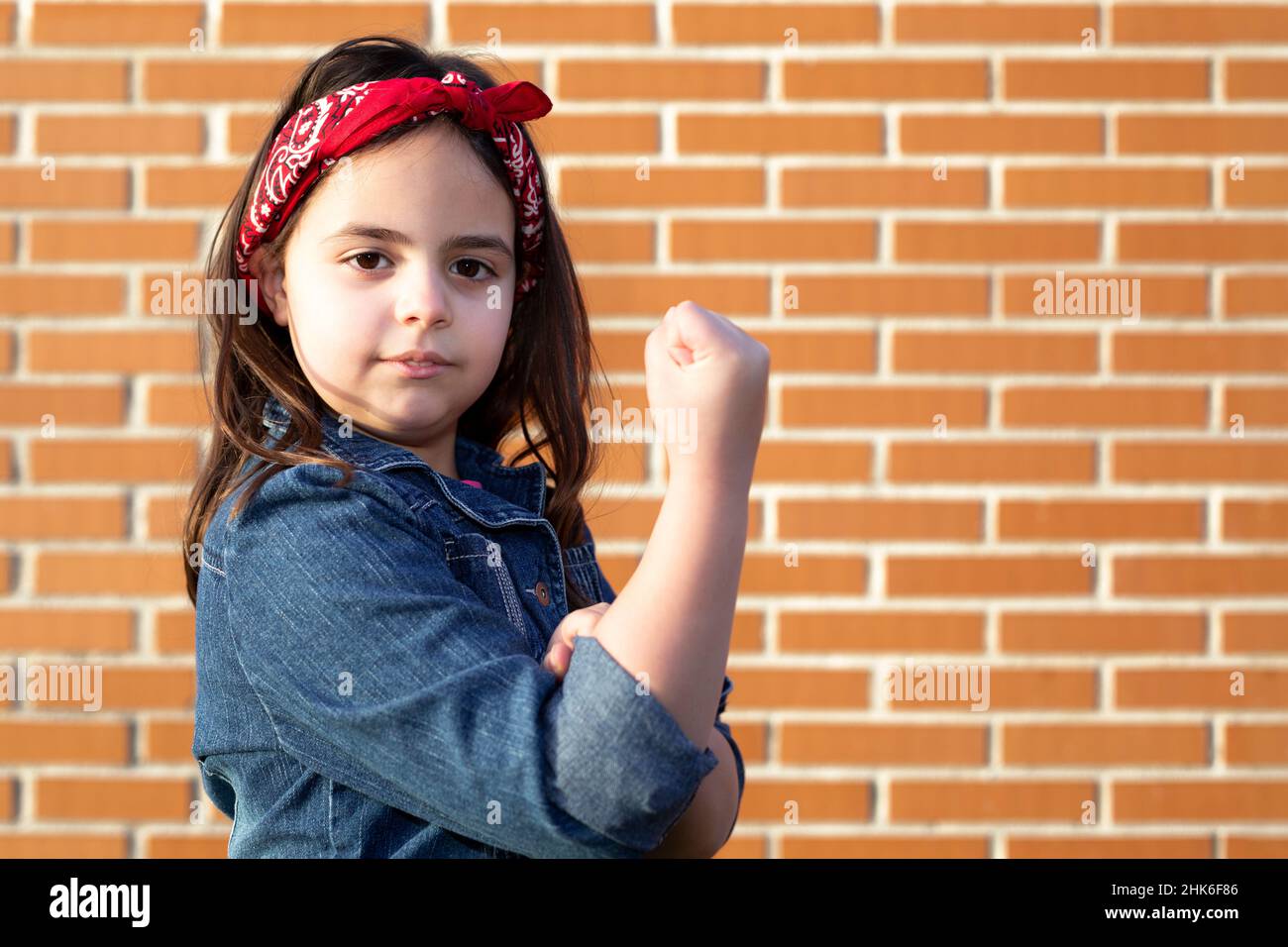 Little girl in clothing representative of working woman isolated on brick wall. Space for text. Stock Photo